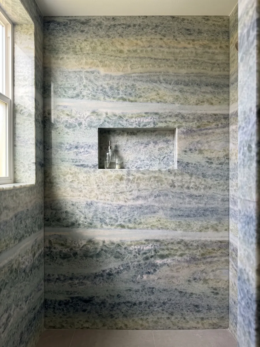 Ducha revestida con placas enteras de mármol azul Calcite Caraibica con nicho empotrado: bandas horizontales de cristales gris azulado, verde salvia y beige