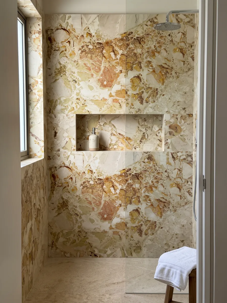 Ducha revestida con placas enteras de mármol beige Alma Fuoco con nicho empotrado: manchas ocre y óxido de bordes recortados que se agrupan en la parte superior central