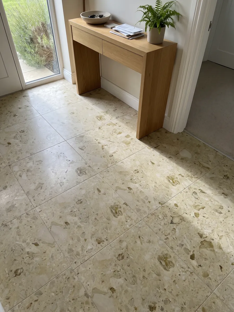 Piso de recibidor en placas grandes de mármol beige Alma con luz natural: fondo crema verdoso con inclusiones fósiles oliva dispersas y suaves