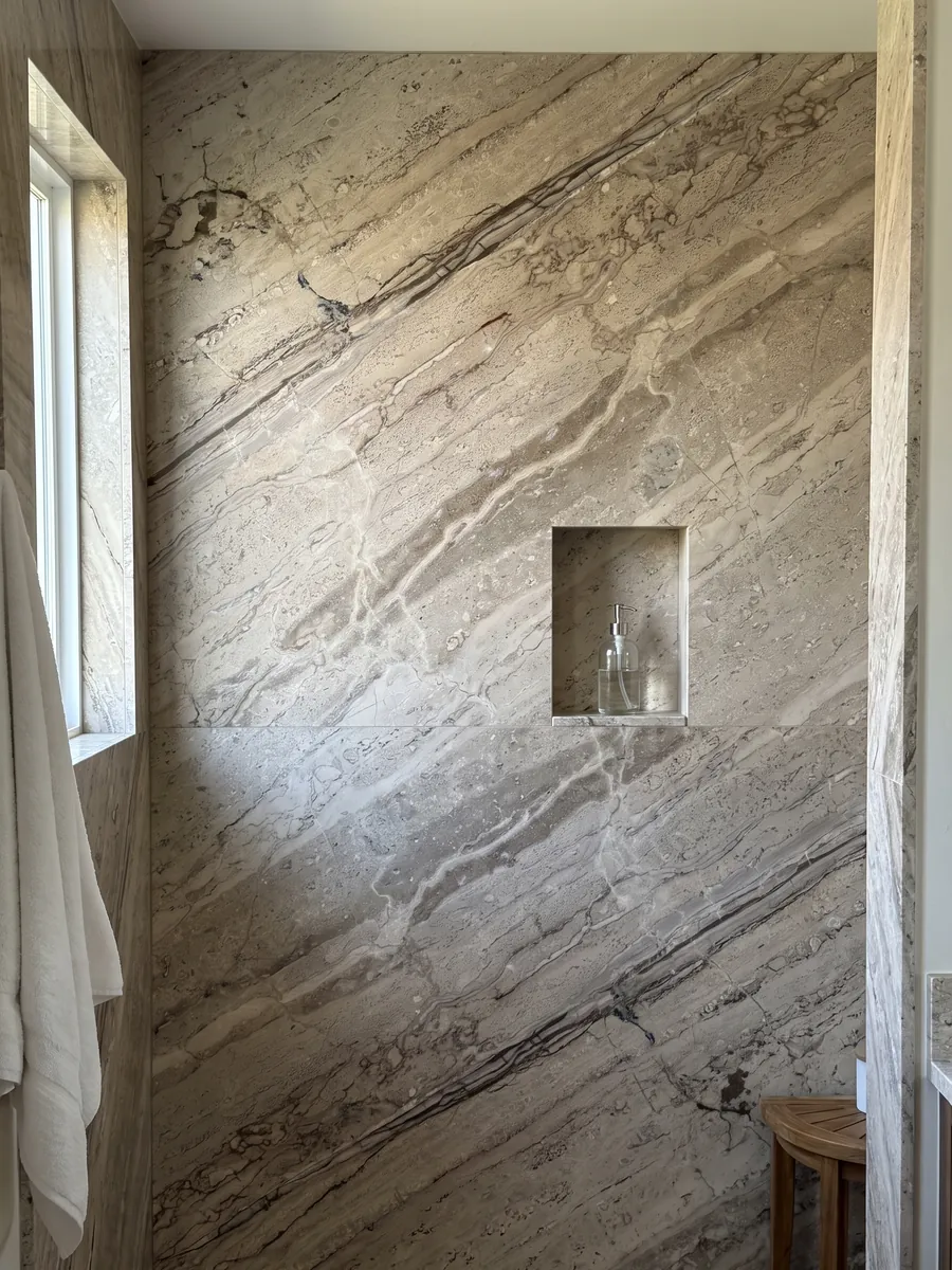 Ducha revestida con placas enteras de mármol beige Breccia Aurora con nicho empotrado: beige grisáceo con vetas paralelas marrones en diagonal y zona más rayada abajo