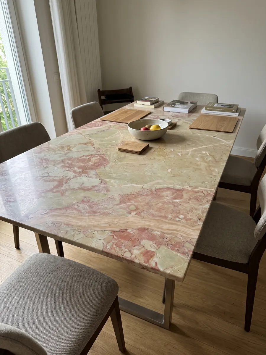 Mesa de comedor con cubierta de mármol beige Breccia D’Aragona sobre base de acero: fragmentos beige verdosos grandes con manchas rosa coral en el borde izquierdo