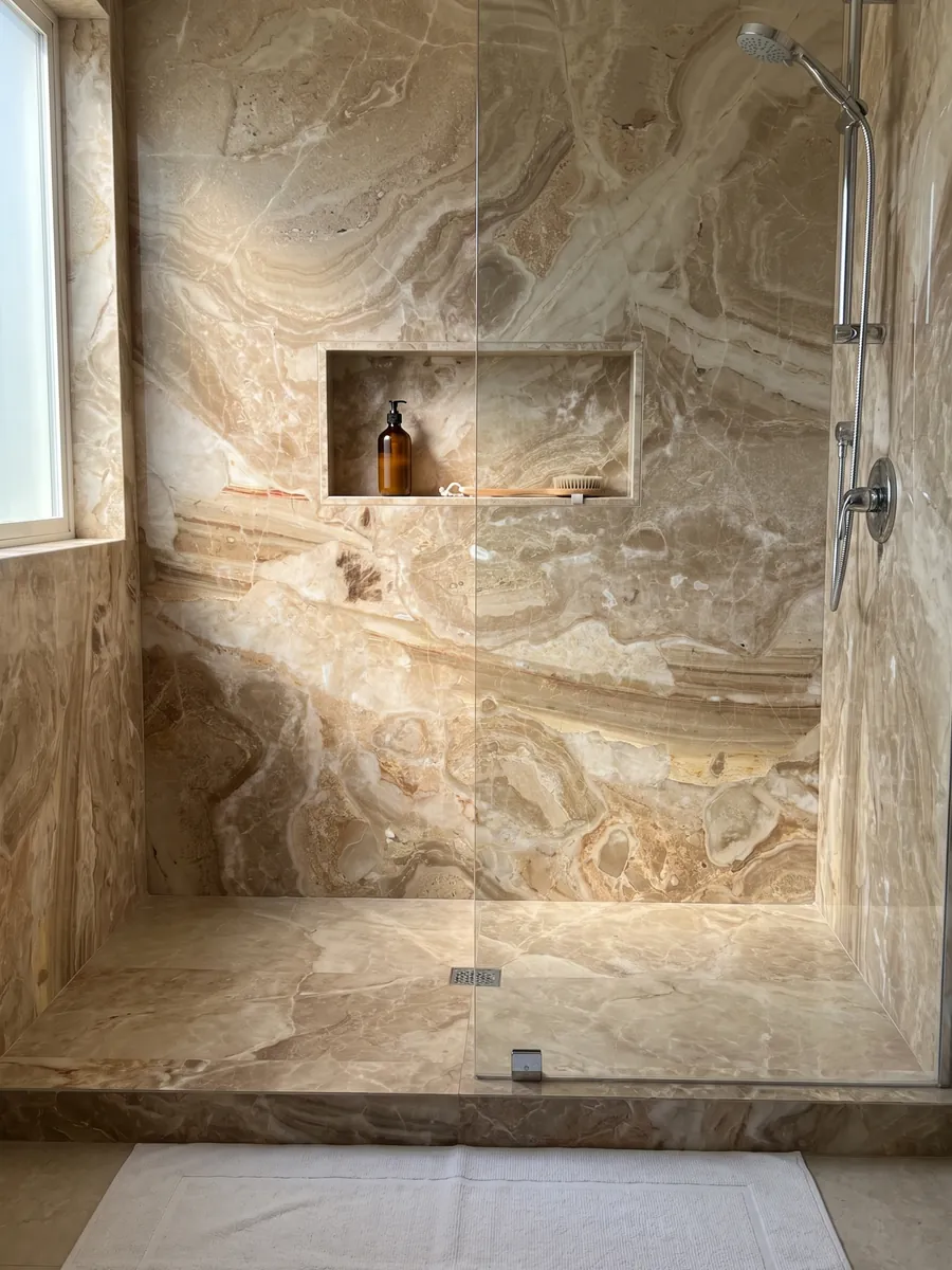 Ducha revestida con placas enteras de mármol beige Breccia Oniciata con nicho empotrado: fragmentos beige dorado con ondas concéntricas y una banda marrón rayada abajo