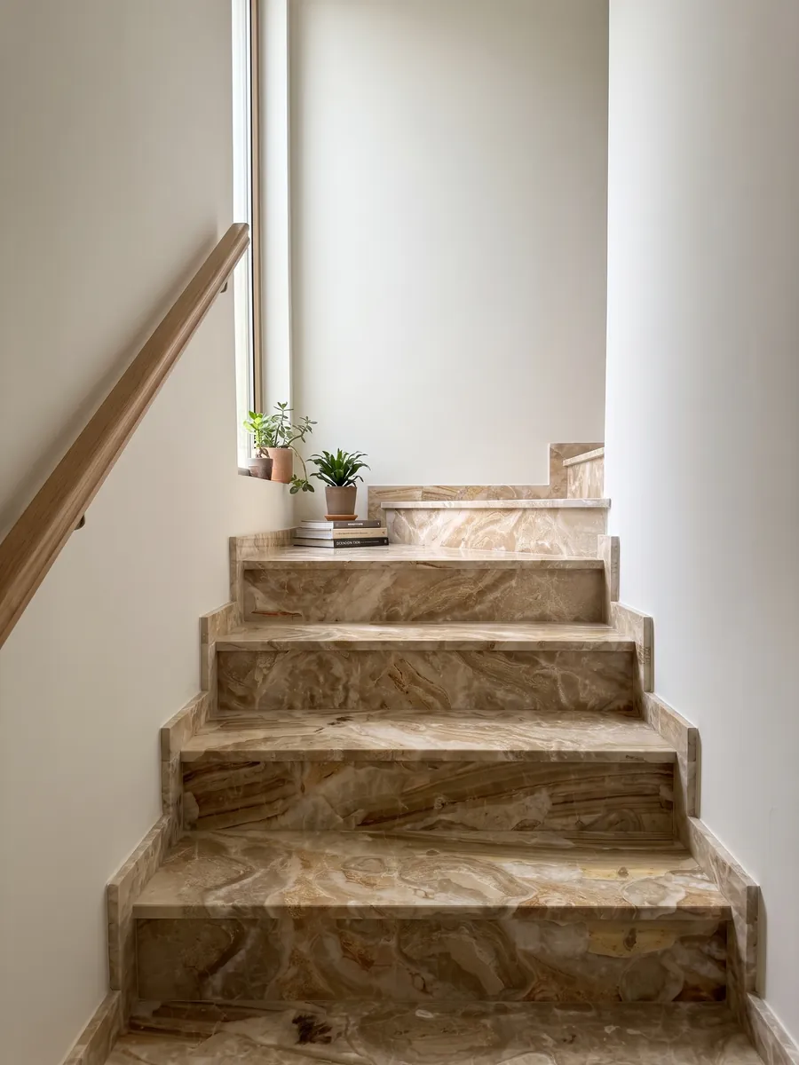 Escalera interior con peldaños de mármol beige Breccia Oniciata con pasamanos: fragmentos beige dorado con ondas concéntricas y una banda marrón rayada abajo