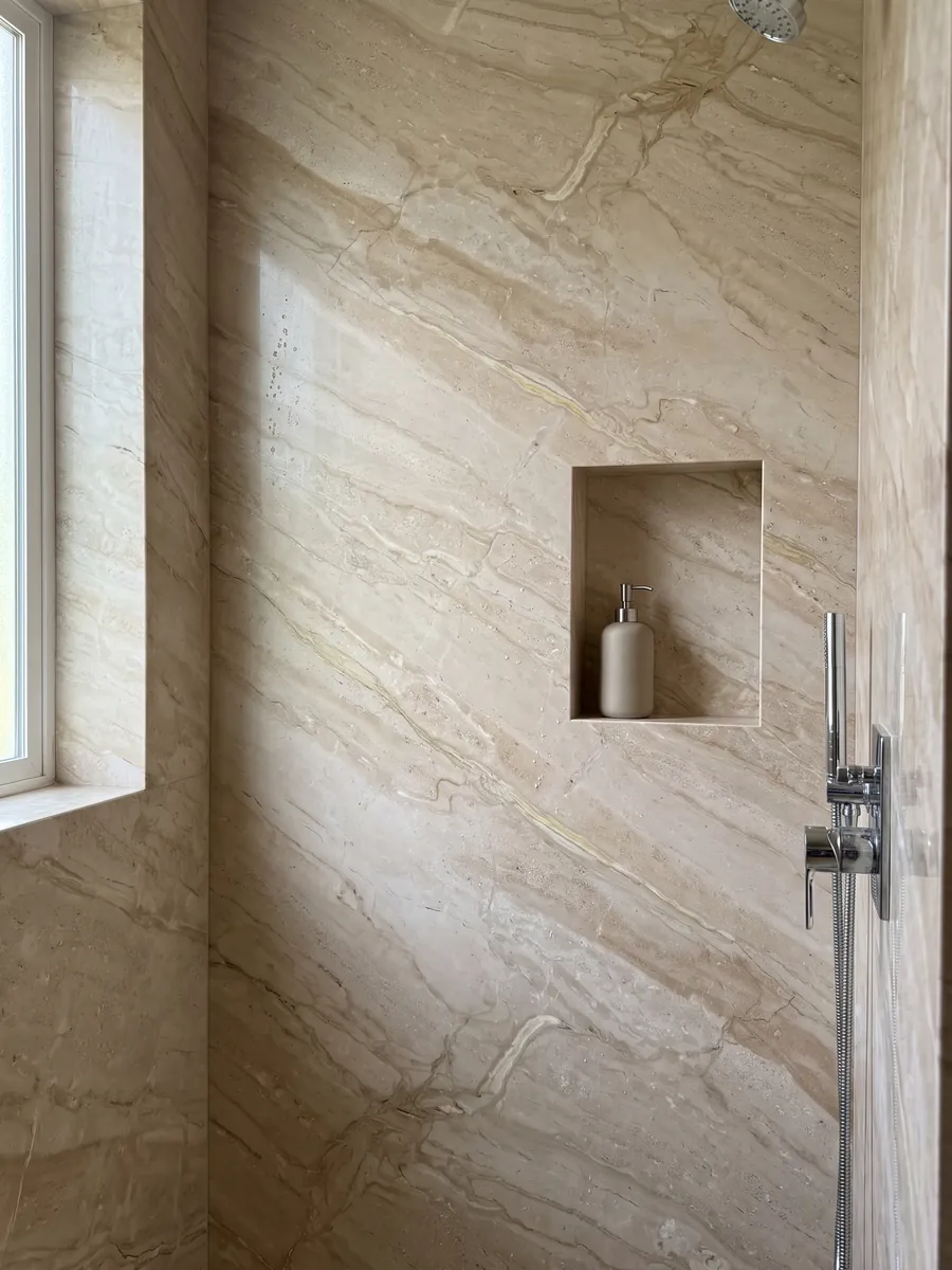 Ducha revestida con placas enteras de mármol beige Breccia Sarda con nicho empotrado: beige cálido con vetas crema y marrón claro en diagonal