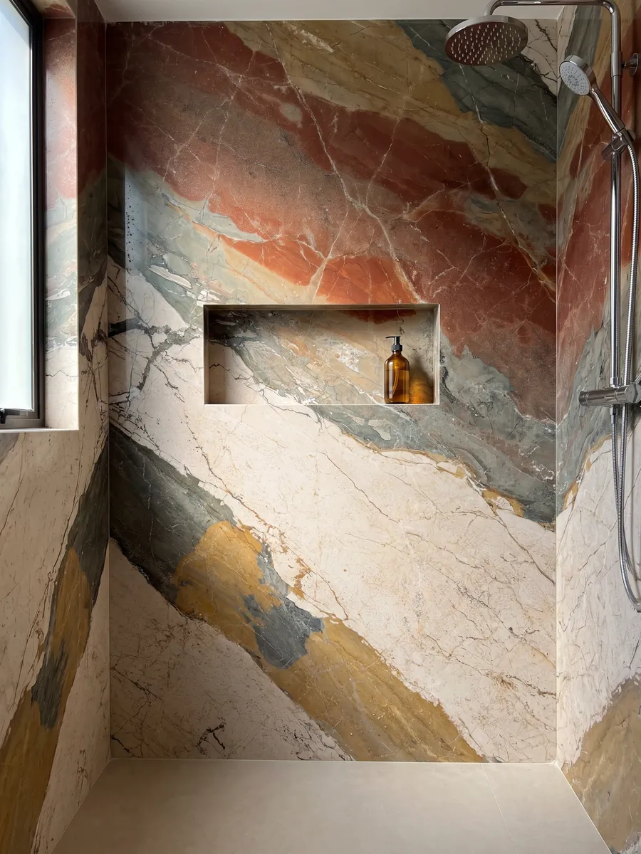 Ducha revestida con placas enteras de mármol beige Etna con nicho empotrado: franjas diagonales de cuatro colores muy distintos: crema, gris verdoso, ocre y rojo óxido
