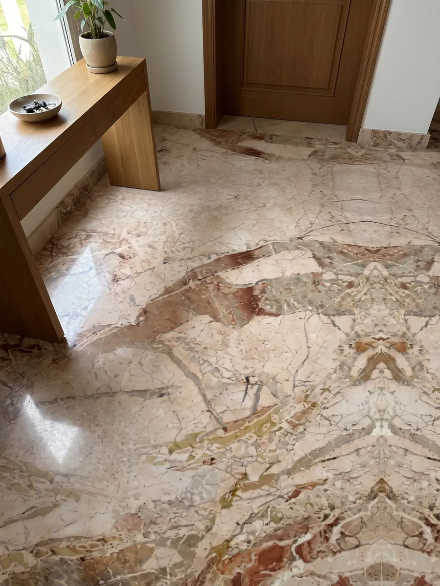 Piso de recibidor en placas grandes de mármol beige Golden Vein con luz natural: fragmentos beige rosado separados por manchas terracota; el dibujo parece reflejado en espejo