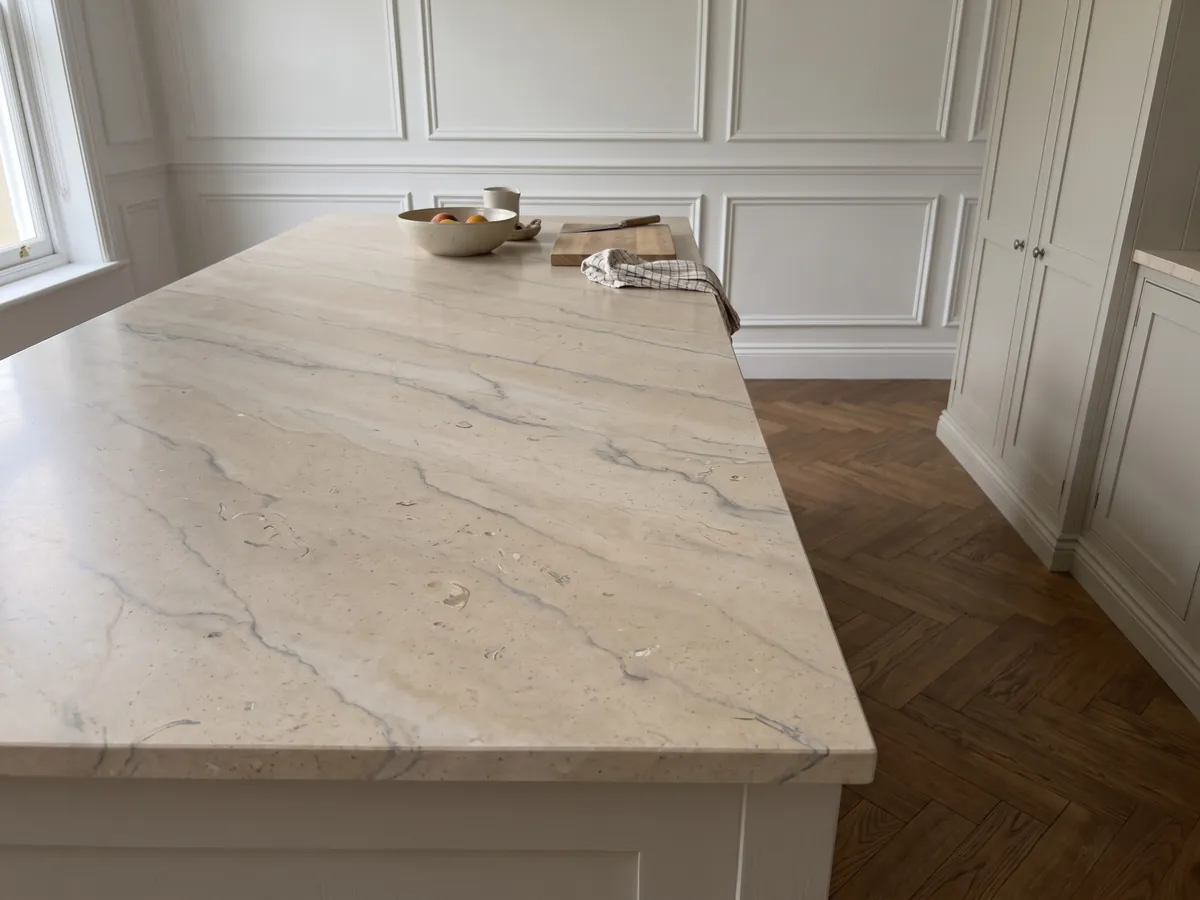 Isla de cocina con cubierta de Mármol Beige Maya y canto recto en una cocina con luz natural: beige cálido con vetas grises suaves y pequeños fósiles