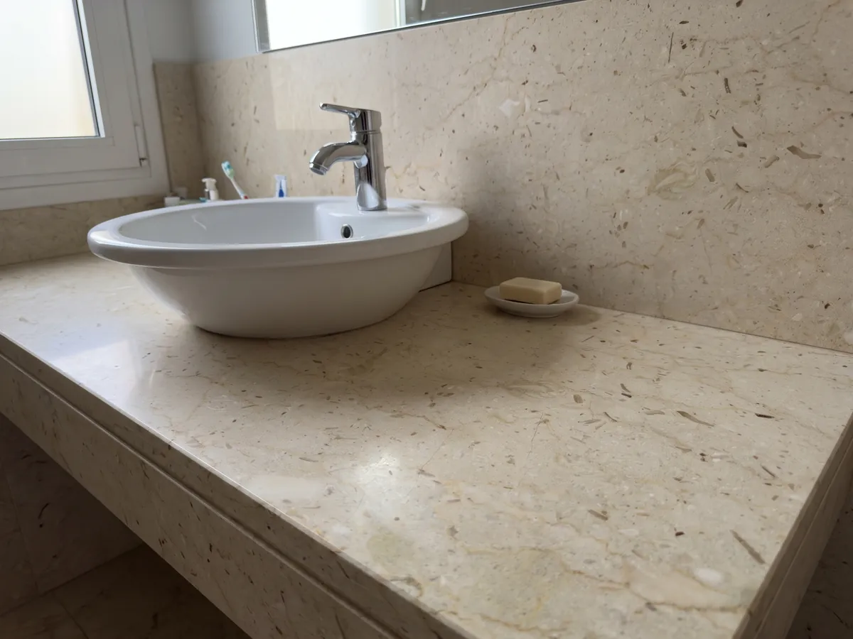 Cubierta de lavabo y pared de baño en mármol beige Pietra Ducale con lavamanos blanco y grifería cromada: crema amarillento con pequeños fragmentos fósiles y puntitos marrones