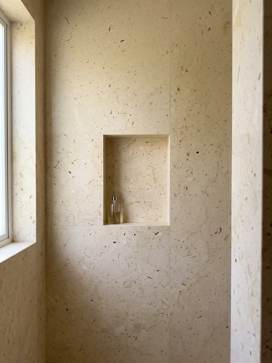 Ducha revestida con placas enteras de mármol beige Pietra Ducale con nicho empotrado: crema amarillento con pequeños fragmentos fósiles y puntitos marrones
