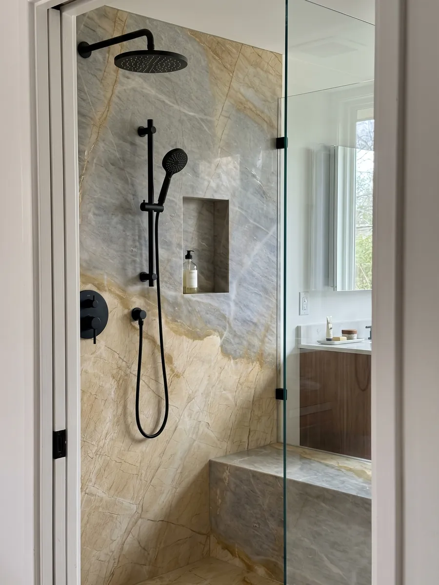 Ducha revestida con placas enteras de mármol beige Skysand con nicho empotrado: una zona amarillo dorado y otra gris azulada separadas por una línea ocre