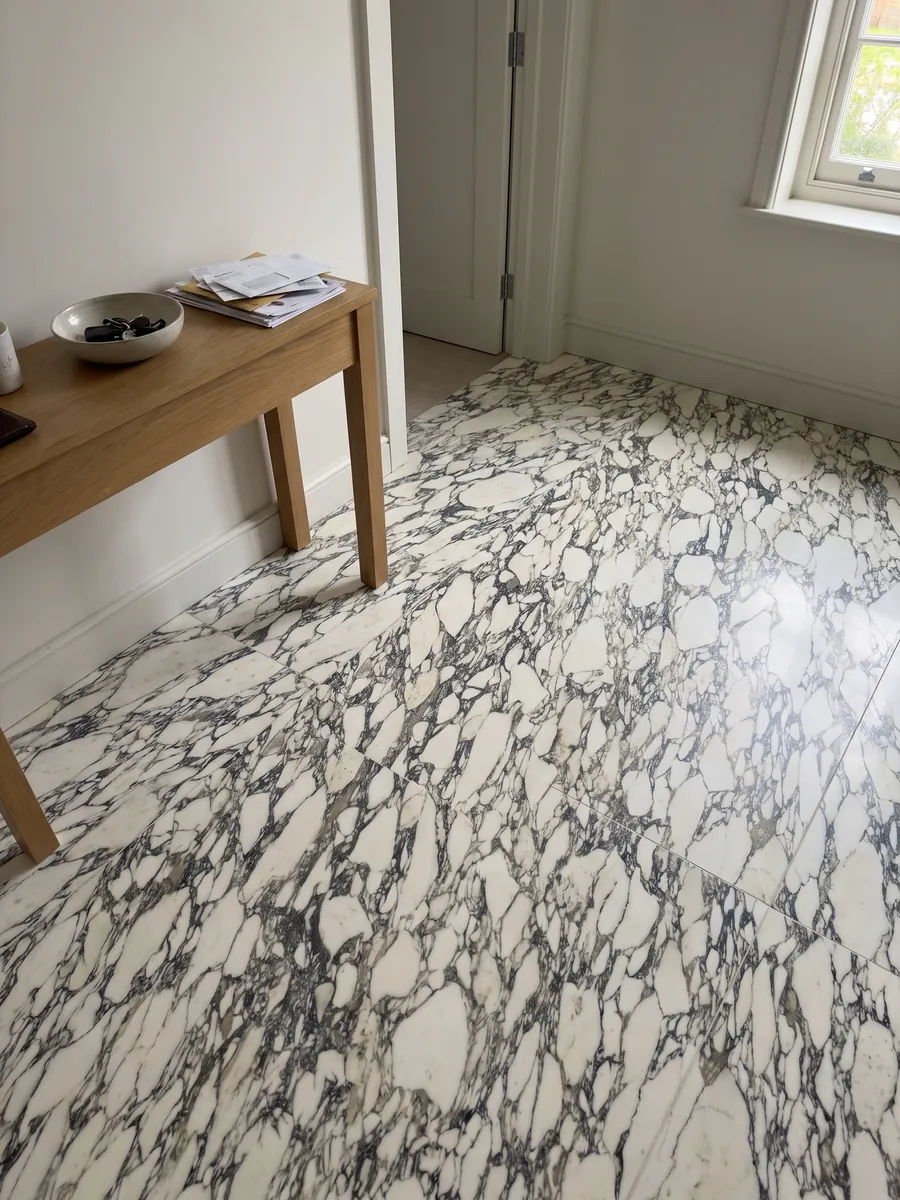 Piso de recibidor en placas grandes de mármol blanco Arabescato Corchia con luz natural: red muy densa de vetas oscuras finas que encierran muchos fragmentos blancos pequeños
