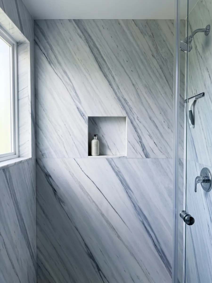 Ducha revestida con placas enteras de mármol blanco Bianco Covelano con nicho empotrado: vetas rectas gris azulado en diagonal y paralelas sobre blanco