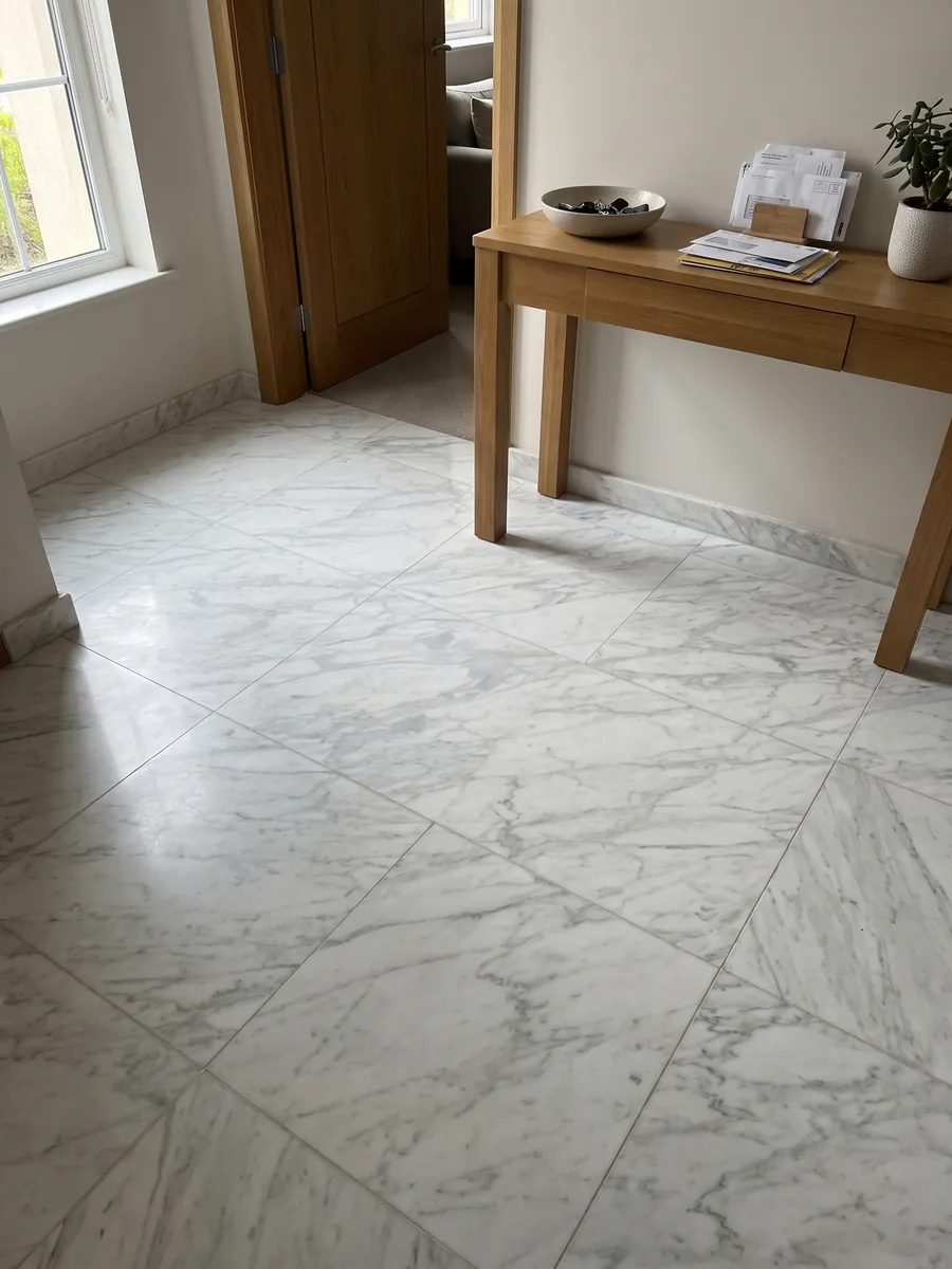 Piso de recibidor en placas grandes de mármol blanco Calacatta Classic con luz natural: blanco con vetas gris claro finas en diagonal sobre toda la placa