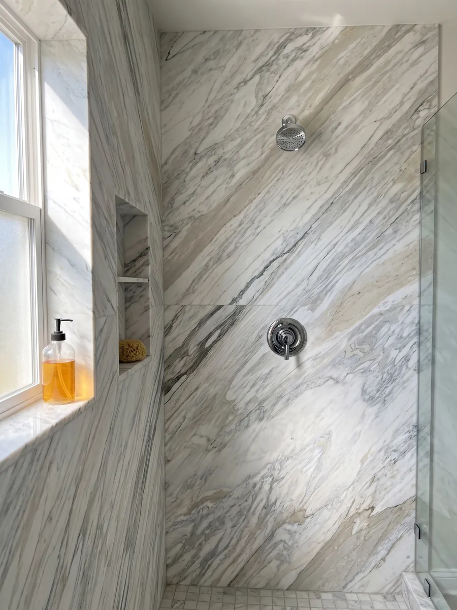 Ducha revestida con placas enteras de mármol blanco Calacatta Manhattan con nicho empotrado: blanco con vetas grises finas y suaves que fluyen en diagonal