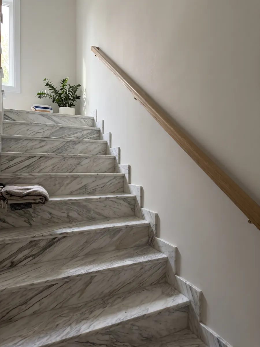 Escalera interior con peldaños de mármol blanco Calacatta Manhattan con pasamanos: blanco con vetas grises finas y suaves que fluyen en diagonal