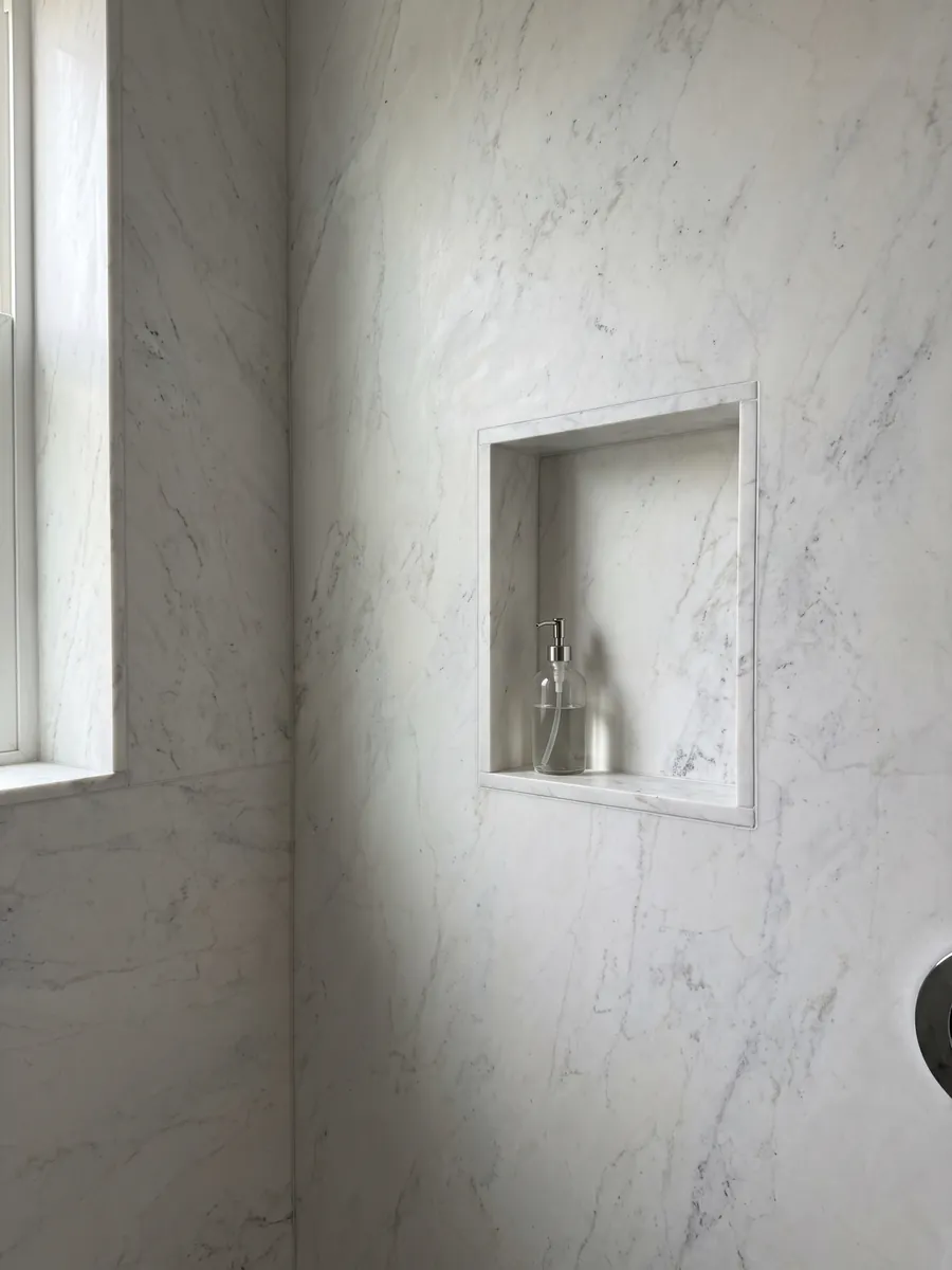 Ducha revestida con placas enteras de mármol blanco Calacatta Michelangelo con nicho empotrado: blanco grisáceo casi liso con pocas marcas grises muy suaves