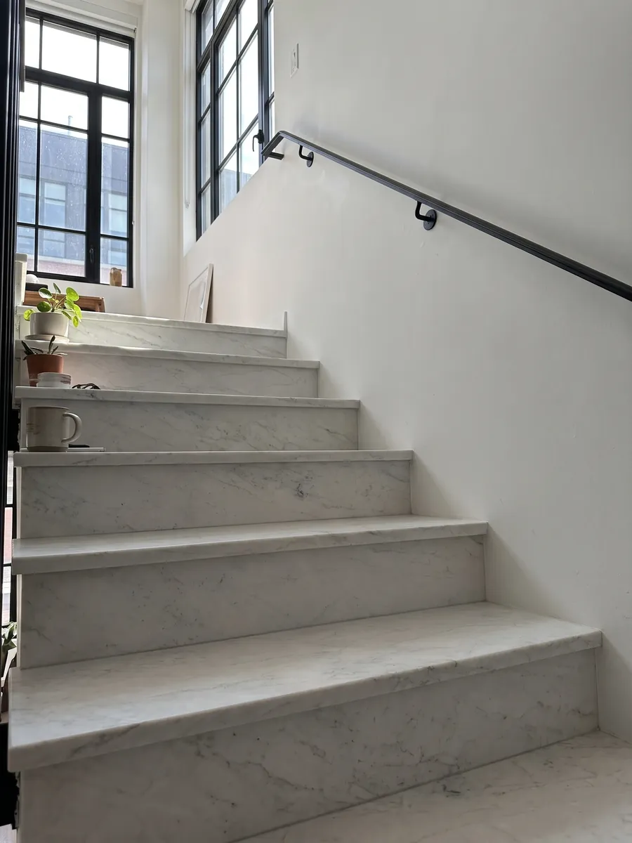 Escalera interior con peldaños de mármol blanco Calacatta Michelangelo con pasamanos: blanco grisáceo casi liso con pocas marcas grises muy suaves