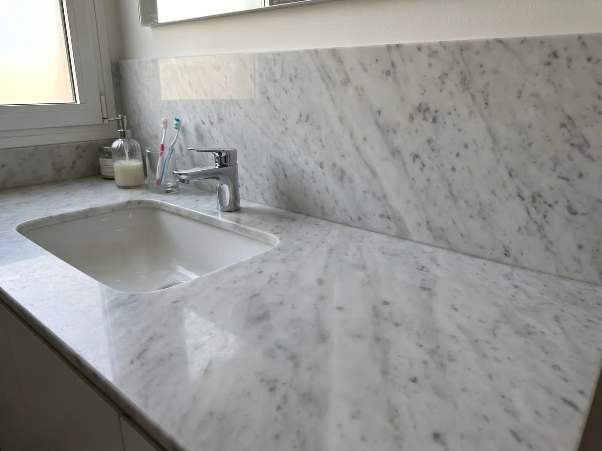 Cubierta de lavabo y pared de baño en mármol blanco Carrara CD con lavamanos blanco y grifería cromada: blanco grisáceo con manchas grises difusas en diagonal