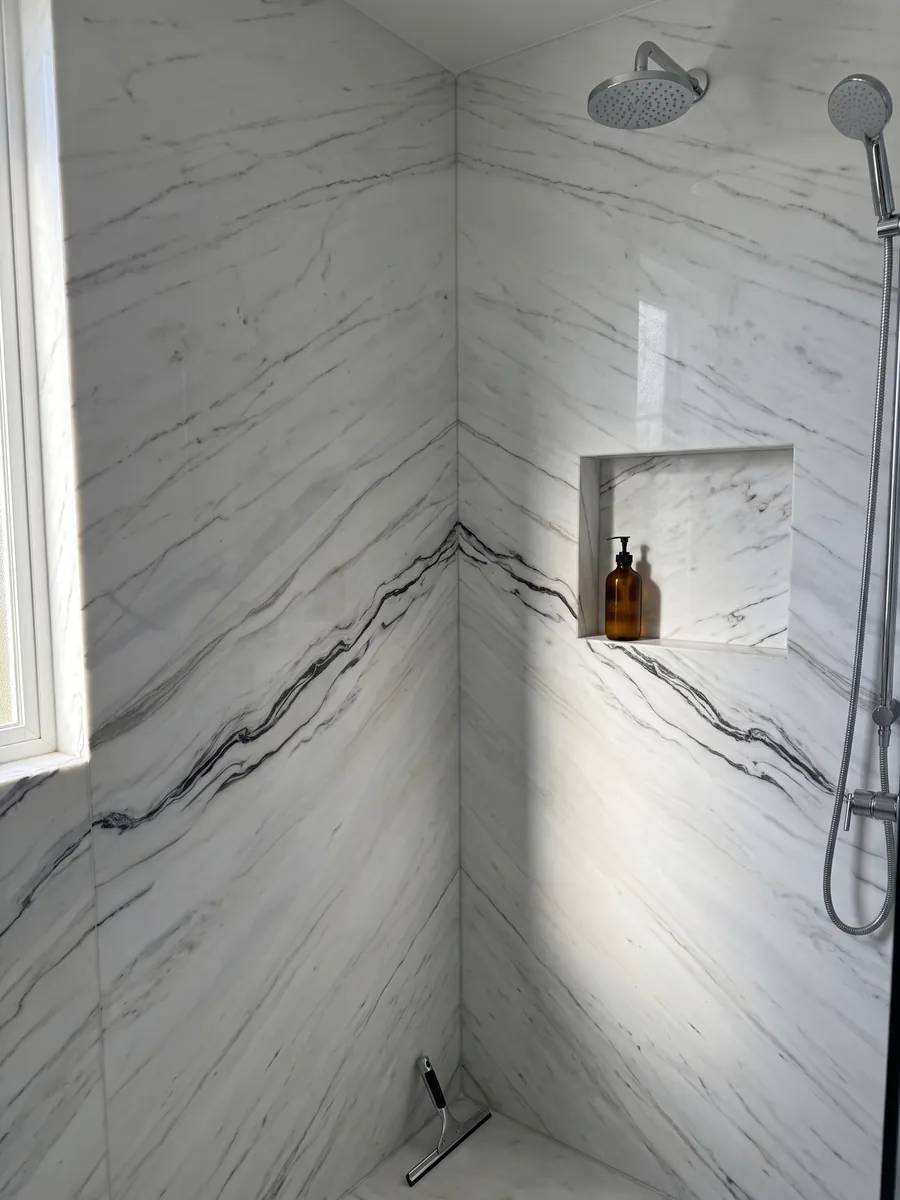 Ducha revestida con placas enteras de Mármol Blanco Covelano Macchia Vecchia con nicho empotrado: blanco con una veta negra ondulada que atraviesa la placa casi horizontalmente