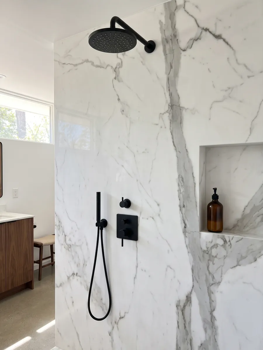 Ducha revestida con placas enteras de mármol blanco Geneva con nicho empotrado: blanco muy limpio cruzado por una veta gris vertical y algunas ramas finas