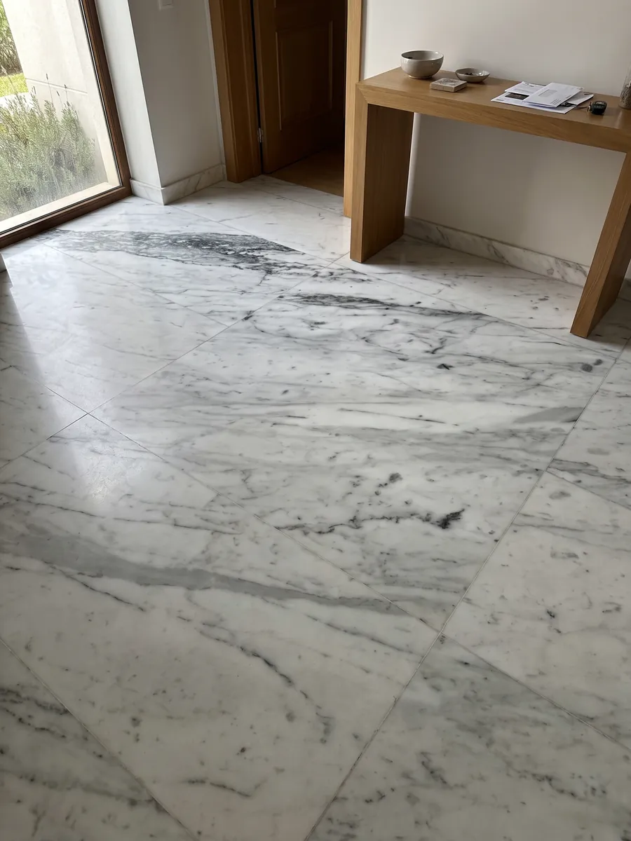 Piso de recibidor en placas grandes de Mármol Blanco Gioia con luz natural: blanco con vetas grises en diagonal, más densas y oscuras en la parte superior
