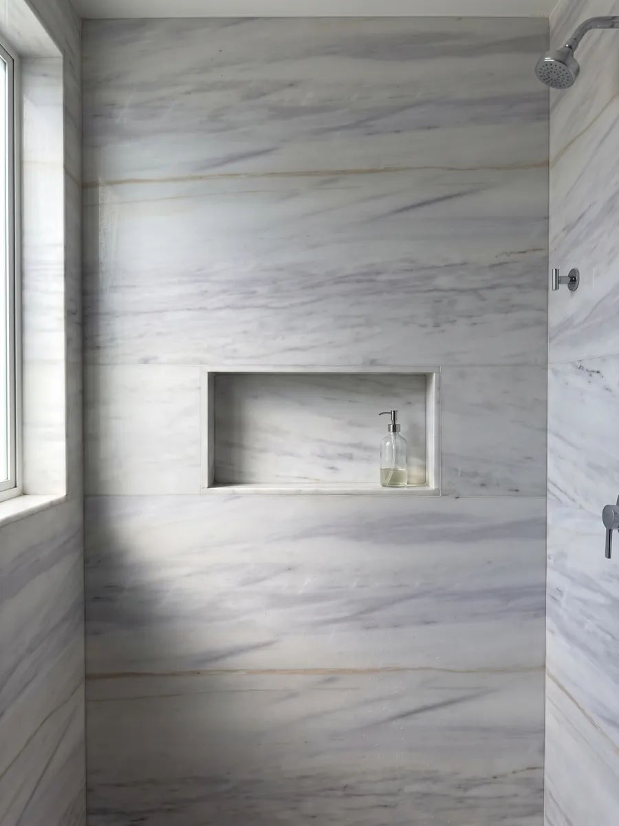 Ducha revestida con placas enteras de Mármol Blanco Lasa Covelano Gold con nicho empotrado: blanco grisáceo con vetas horizontales lavanda suaves y una fina línea dorada