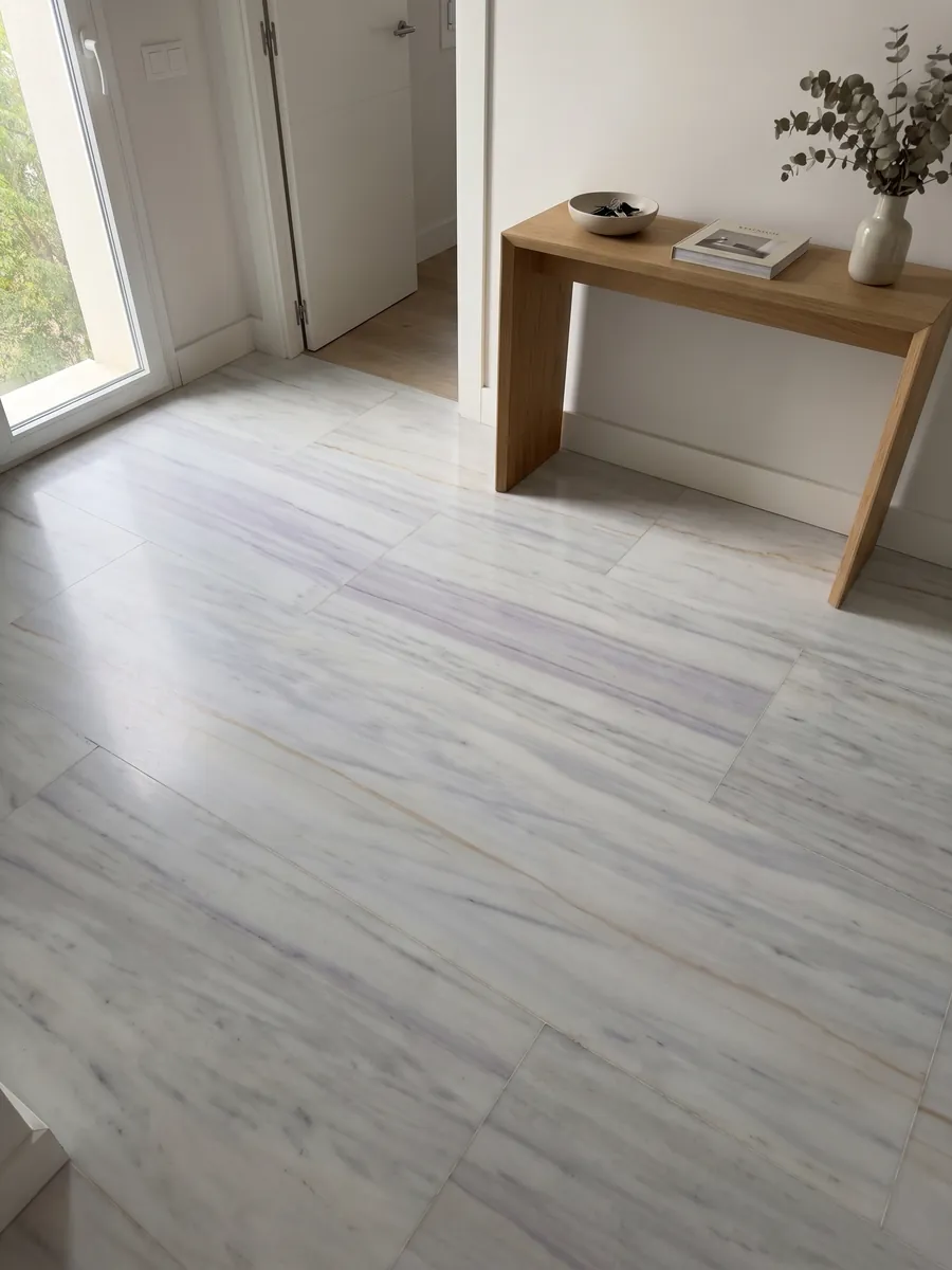 Piso de recibidor en placas grandes de Mármol Blanco Lasa Covelano Gold con luz natural: blanco grisáceo con vetas horizontales lavanda suaves y una fina línea dorada