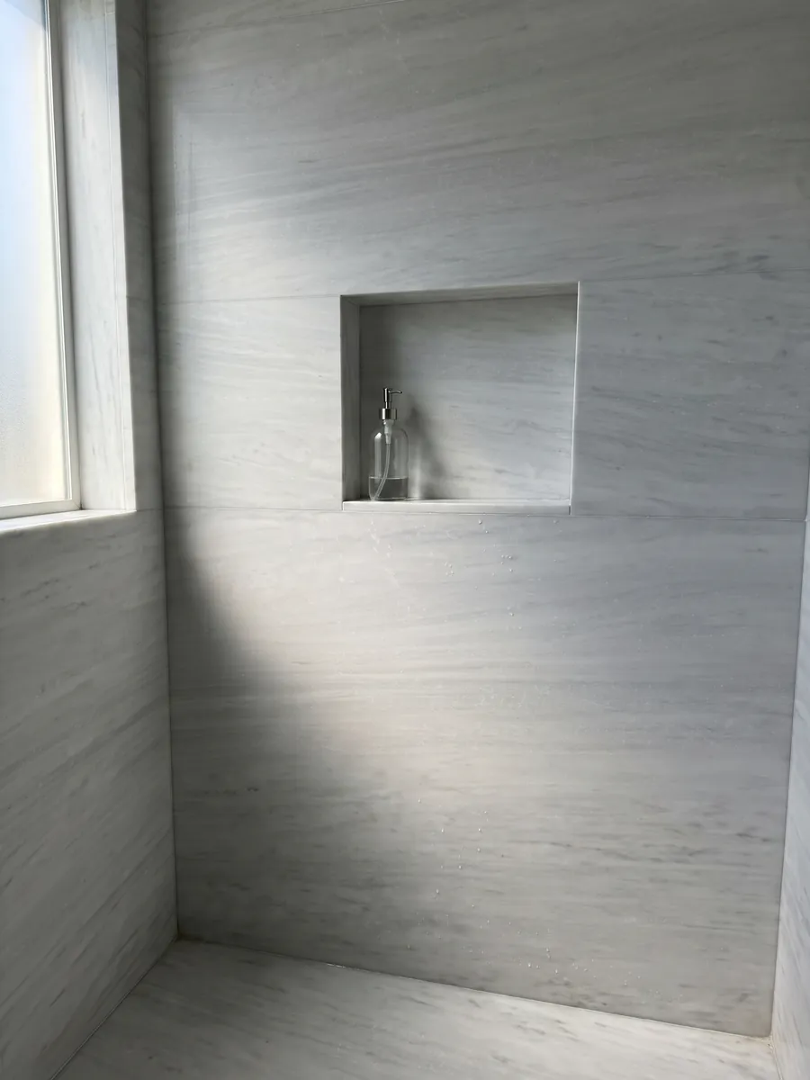 Ducha revestida con placas enteras de Mármol Blanco Laser con nicho empotrado: blanco grisáceo casi liso con líneas horizontales muy suaves