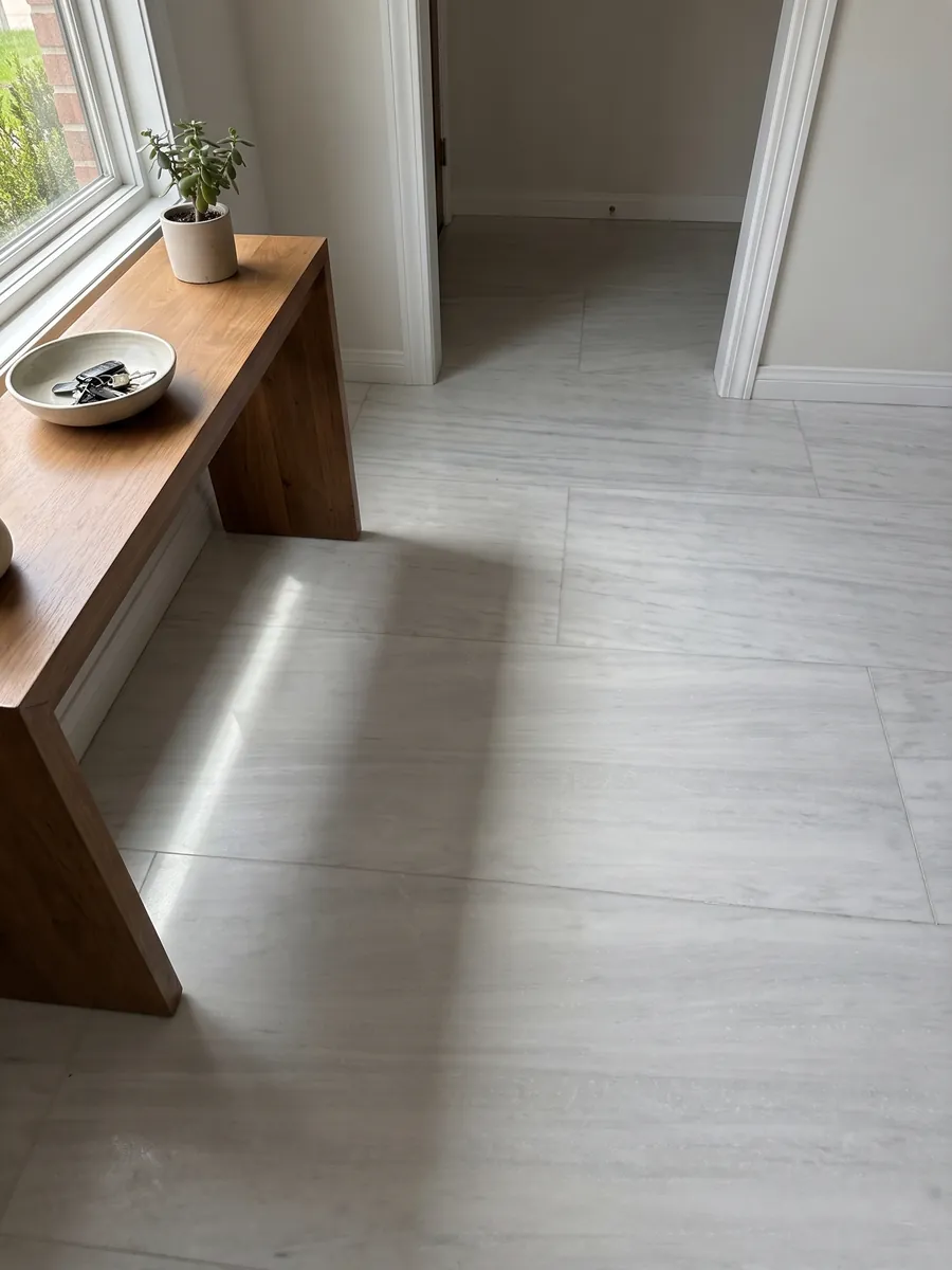 Piso de recibidor en placas grandes de Mármol Blanco Laser con luz natural: blanco grisáceo casi liso con líneas horizontales muy suaves