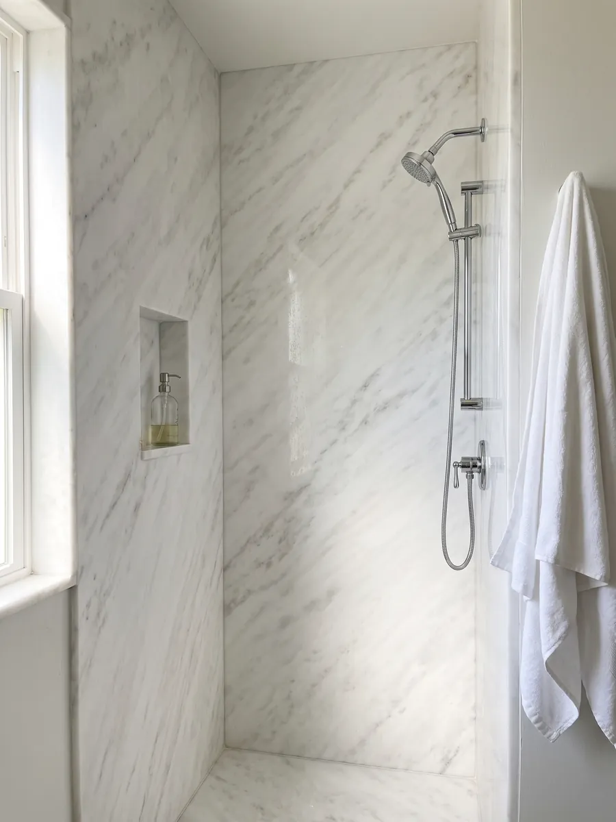 Ducha revestida con placas enteras de mármol blanco Namibia Cream con nicho empotrado: blanco casi liso con nubes grises muy tenues