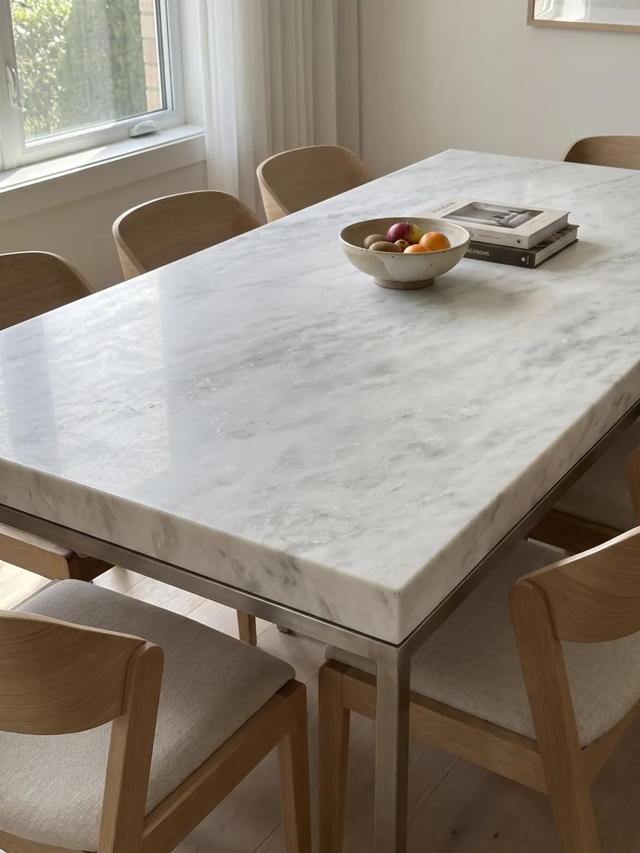Mesa de comedor con cubierta de mármol blanco Namibia Cream sobre base de acero: blanco casi liso con nubes grises muy tenues