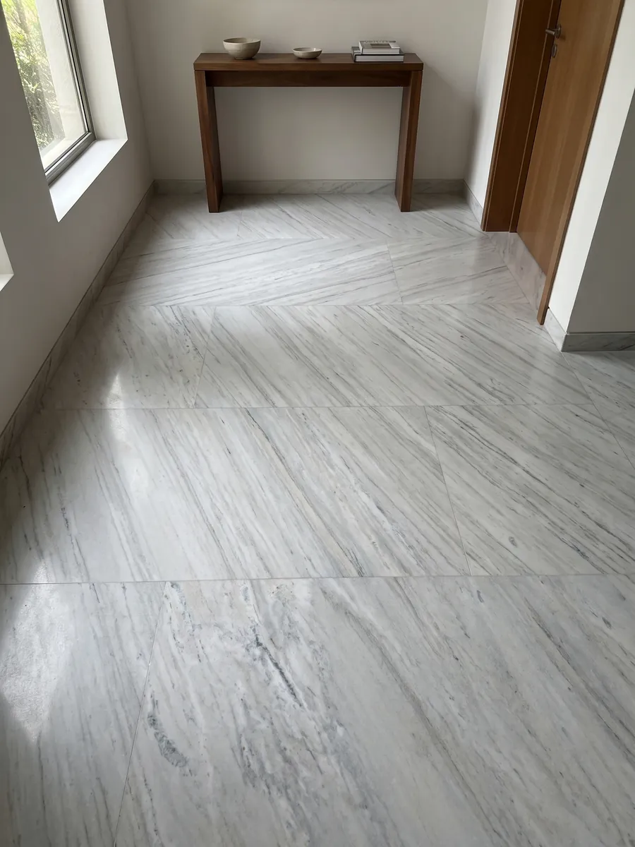 Piso de recibidor en placas grandes de mármol blanco Palissandro con luz natural: blanco grisáceo con trazos grises finos y paralelos en diagonal