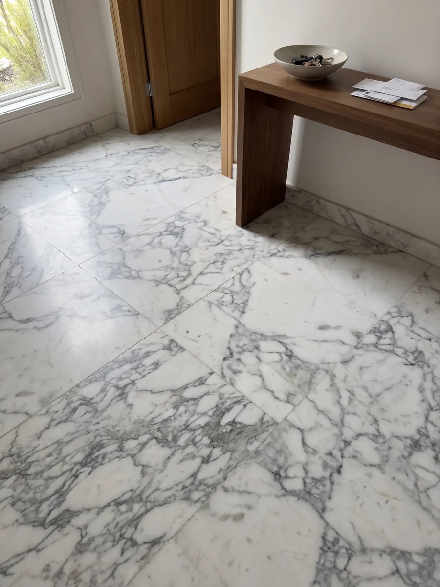 Piso de recibidor en placas grandes de Mármol Blanco Statuarietto con luz natural: blanco con red de vetas grises en fragmentos, concentrada en la parte inferior