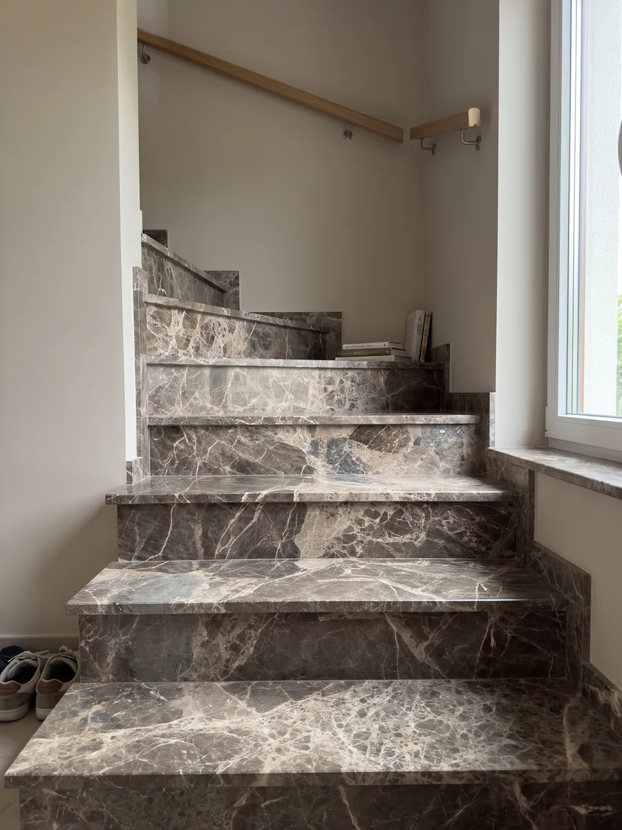 Escalera interior con peldaños de mármol café Breccia Paradiso con pasamanos: fragmentos grandes marrón grisáceo unidos por una red de vetas beige claras