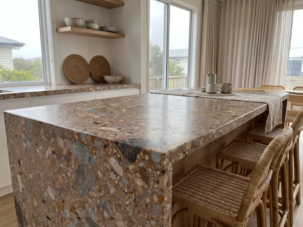Isla de cocina con cubierta de Mármol Ceppo Rojo y canto recto en una cocina con luz natural: matriz marrón rojiza con cantos rodados grises y beige de varios tamaños