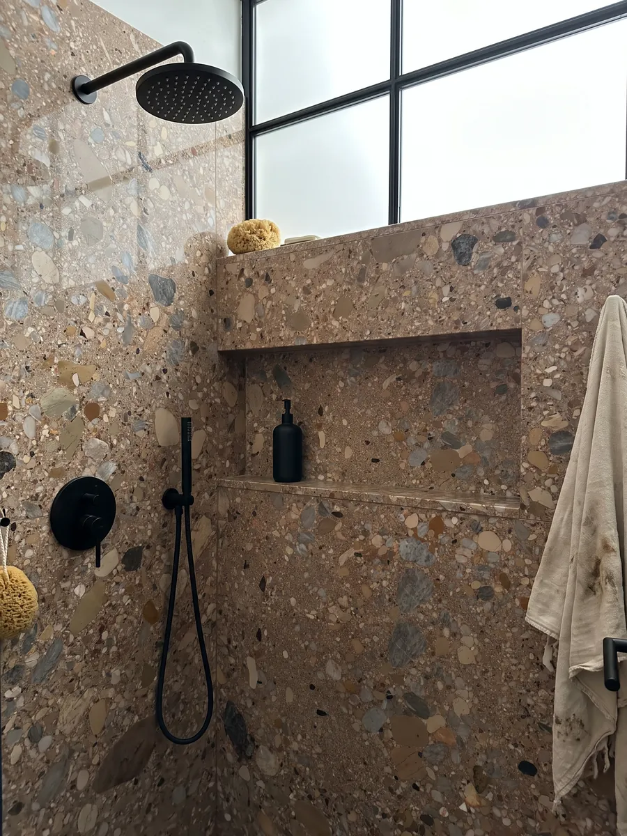 Ducha revestida con placas enteras de Mármol Ceppo Rojo con nicho empotrado: matriz marrón rojiza con cantos rodados grises y beige de varios tamaños