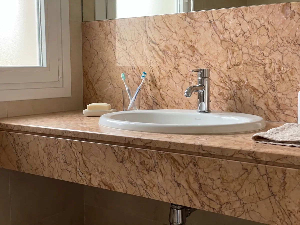 Cubierta de lavabo y pared de baño en Mármol Crema Valencia con lavamanos blanco y grifería cromada: salmón rosado con una red densa de vetas marrones finas