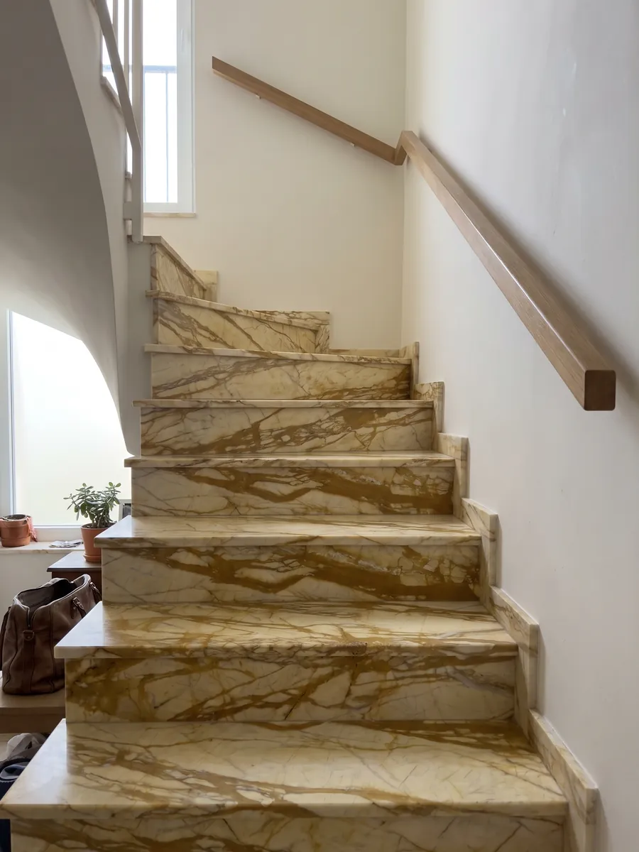 Escalera interior con peldaños de mármol dorado Calacatta Siena con pasamanos: amarillo pálido con red de vetas ocre dorado gruesas en horizontal