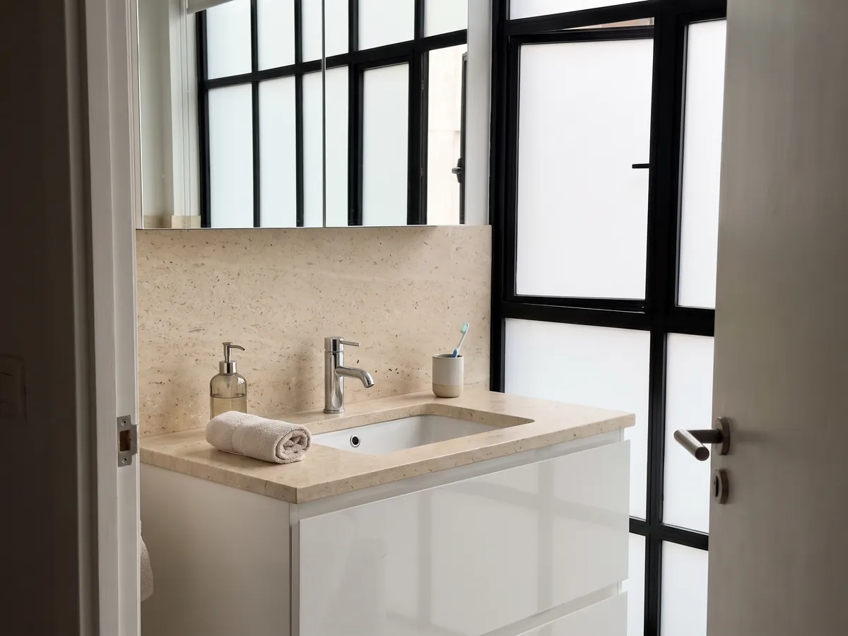 Cubierta de lavabo y pared de baño en Mármol Fior di Crema con lavamanos blanco y grifería cromada: superficie crema muy pareja, de grano fino y sin vetas visibles