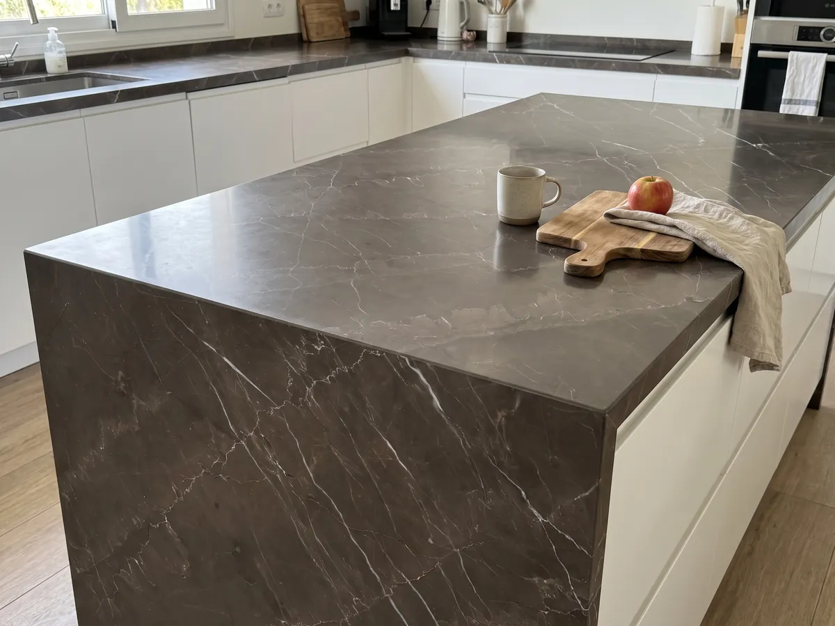 Isla de cocina con cubierta de Mármol Gris Amani y canto recto en una cocina con luz natural: fondo topo oscuro cruzado por vetas blancas finas en diagonal
