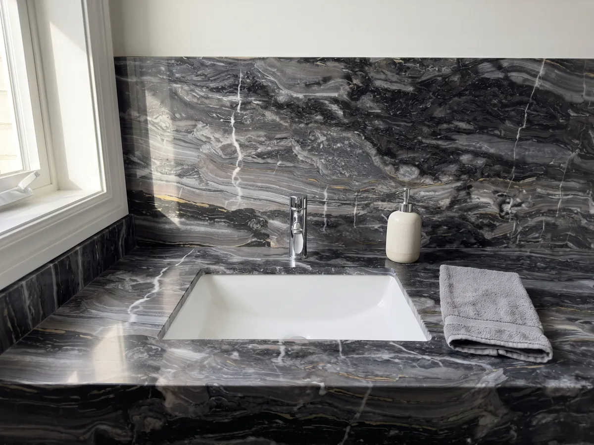 Cubierta de lavabo y pared de baño en mármol gris Arabescato Grigio Orobico: gris antracita con ondas horizontales y algunas vetas blancas finas que lo cortan verticalmente