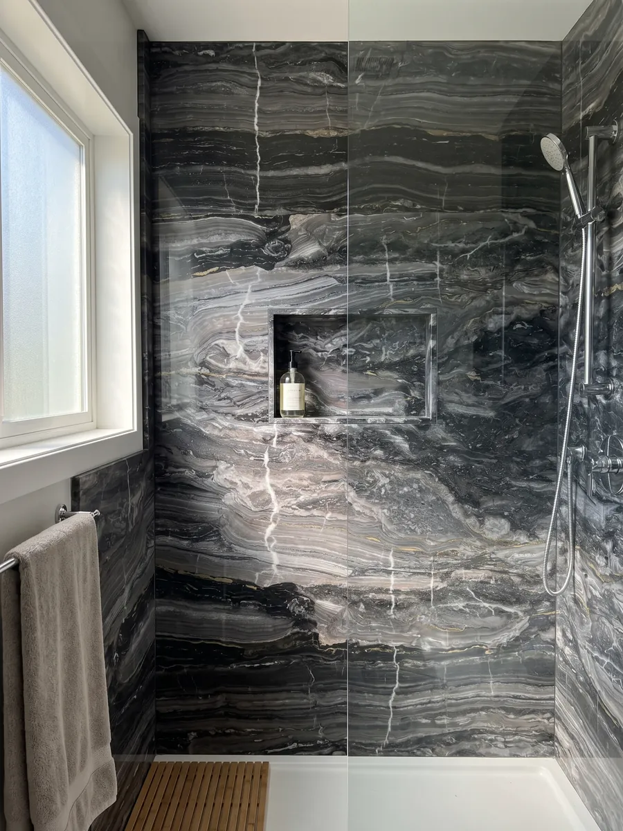 Ducha revestida con placas enteras de mármol gris Arabescato Grigio Orobico con nicho empotrado: gris antracita con ondas horizontales y algunas vetas blancas finas que lo cortan verticalmente