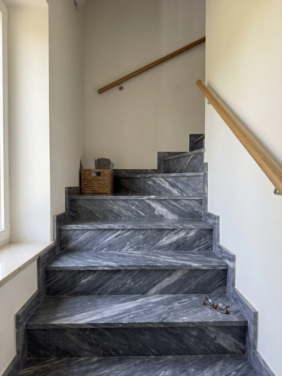 Escalera interior con peldaños de mármol gris Bardiglio Nuvolato con pasamanos: gris oscuro azulado con nubes y vetas blanquecinas difusas en diagonal