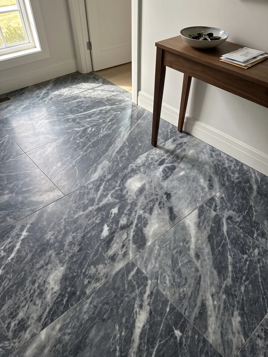Piso de recibidor en placas grandes de mármol gris Bardiglio Nuvolato con luz natural: gris oscuro azulado con nubes y vetas blanquecinas difusas en diagonal