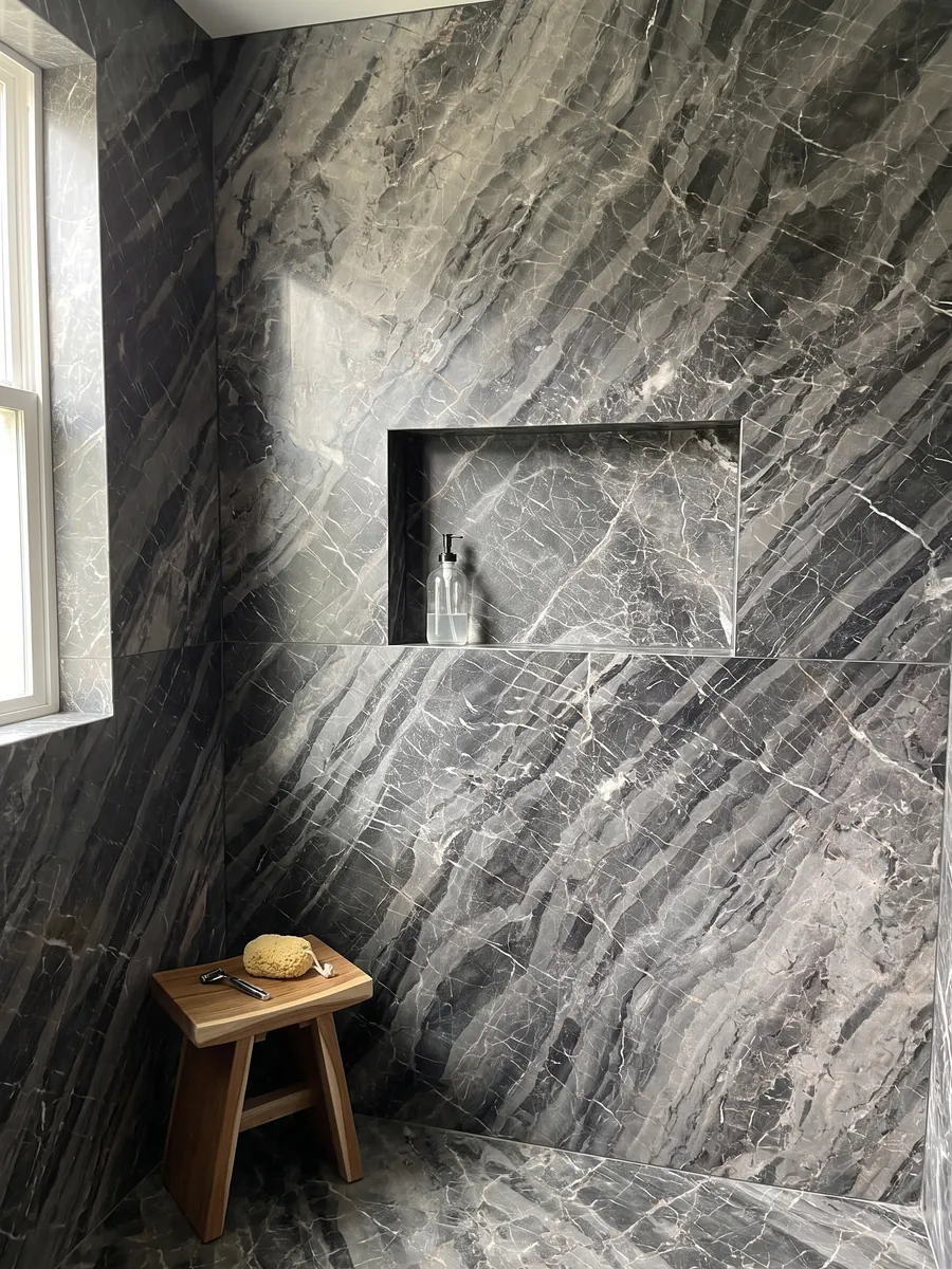 Ducha revestida con placas enteras de mármol gris Bellagio con nicho empotrado: bandas grises diagonales escalonadas con una red de vetas blancas finas