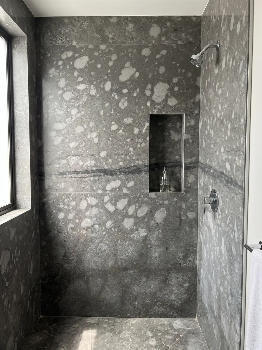 Ducha revestida con placas enteras de Mármol Gris Billiemi con nicho empotrado: gris con manchas claras en forma de nubes y una franja oscura horizontal
