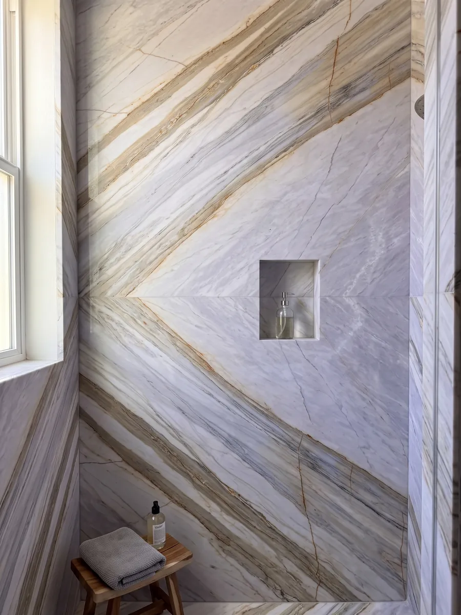 Ducha revestida con placas enteras de mármol gris Calacatta Supreme con nicho empotrado: gris lavanda claro con bandas beige diagonales y finas líneas ocre