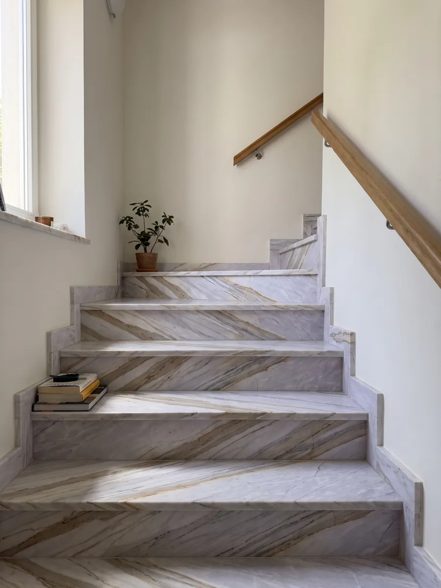 Escalera interior con peldaños de mármol gris Calacatta Supreme con pasamanos: gris lavanda claro con bandas beige diagonales y finas líneas ocre