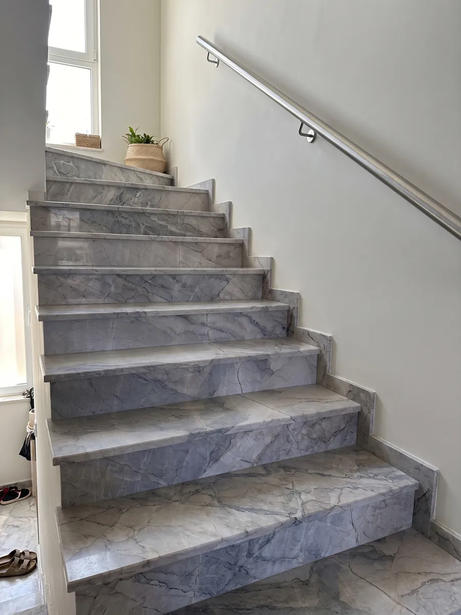 Escalera interior con peldaños de mármol gris Camouflage con pasamanos: fragmentos gris lavanda y azulado con vetas finas en patrón de mosaico
