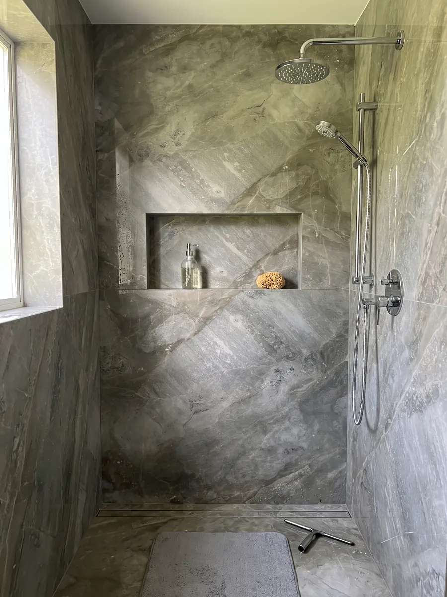 Ducha revestida con placas enteras de mármol gris Fior di Bosco con nicho empotrado: gris verdoso apagado con nubes tonales y vetas finas casi invisibles